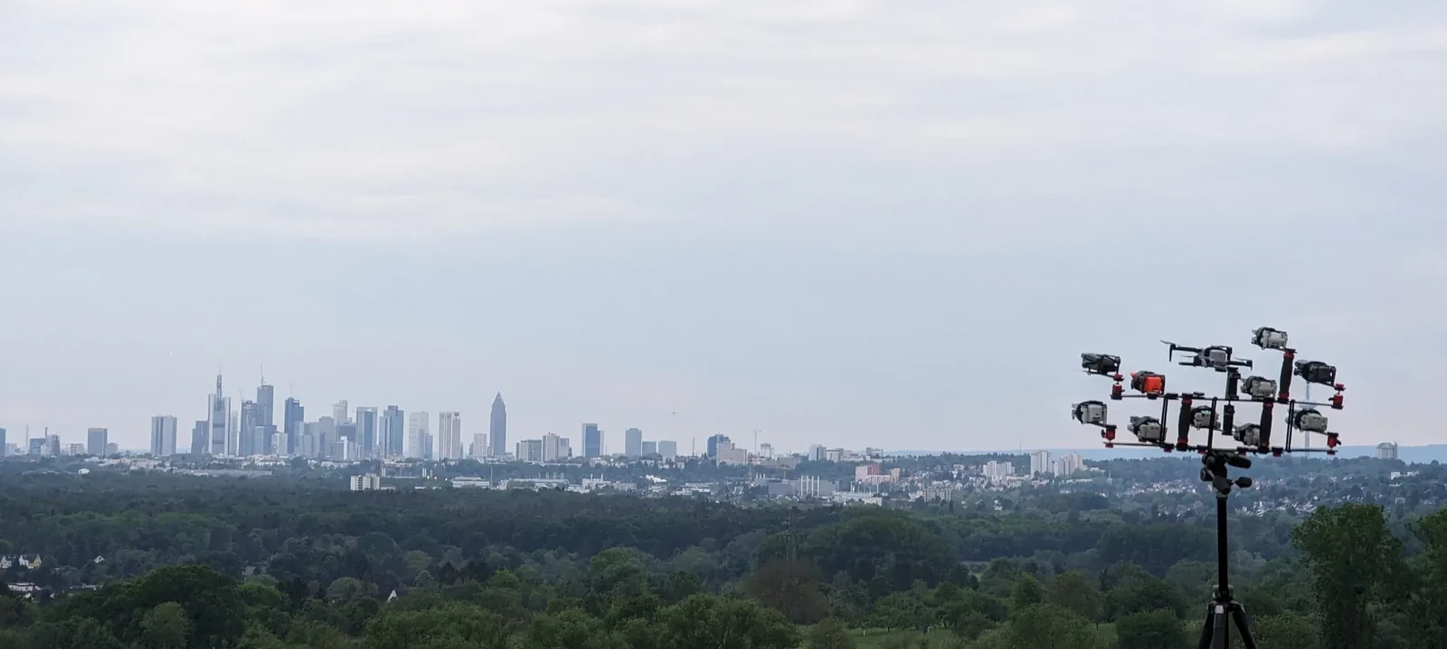 Multiple drones mounted side-by-side on a single tripod rig, pointed at the Frankfurt skyline at sunset